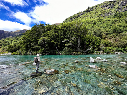 man fishing on rocks by mountainside